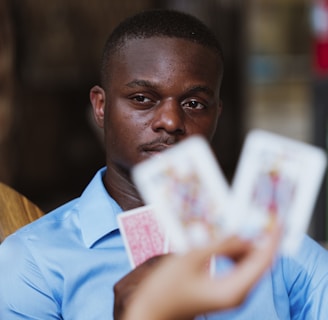 A person wearing a blue shirt is focused intently on playing cards held by someone else. The image highlights a mix of concentration and strategic thinking in a casual setting.