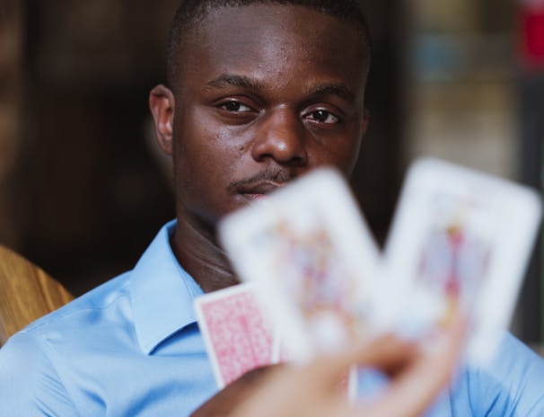 A person wearing a blue shirt is focused intently on playing cards held by someone else. The image highlights a mix of concentration and strategic thinking in a casual setting.